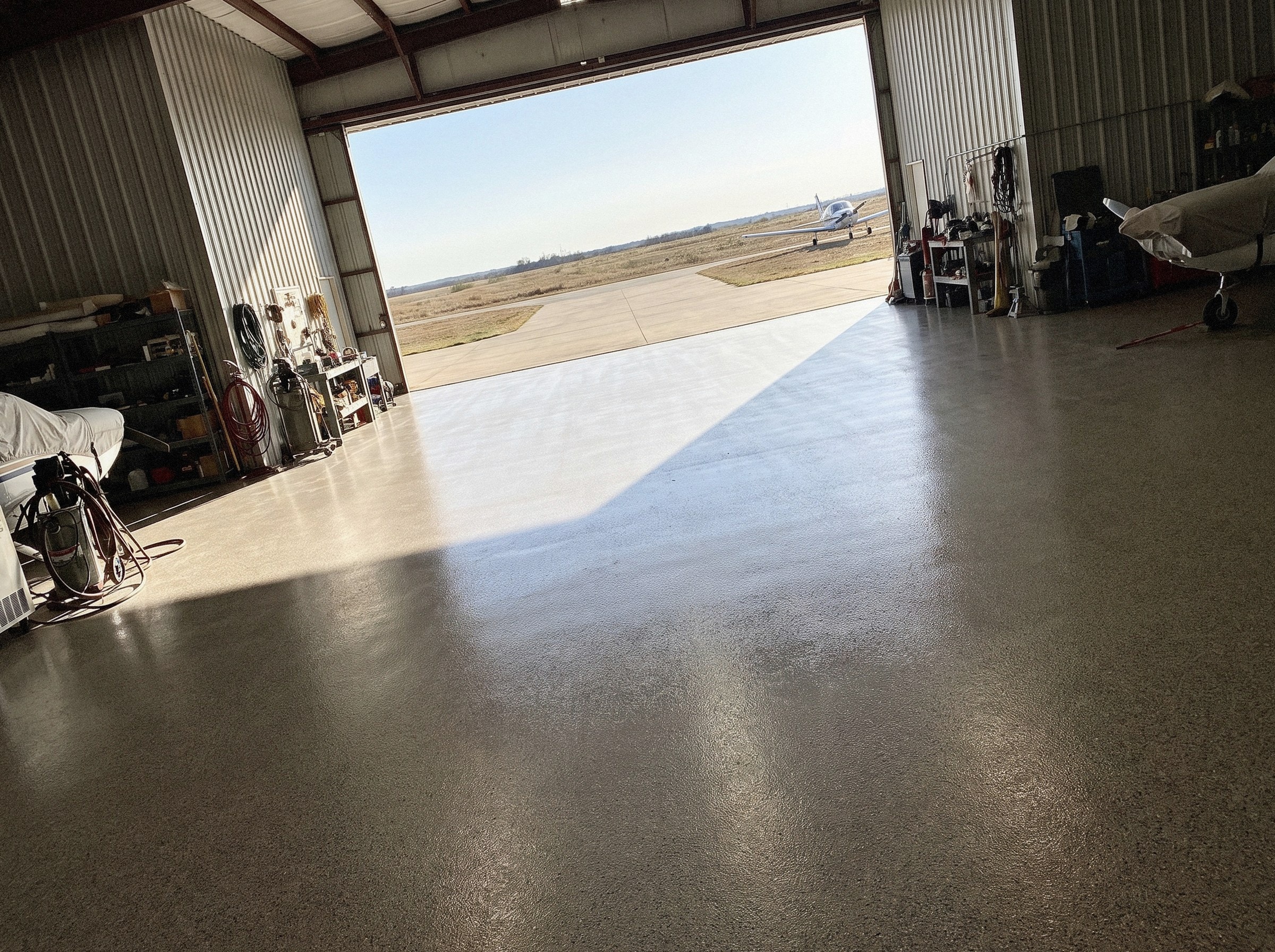 Hangar door standing open, the daylight falling across the coated floor as one long wedge