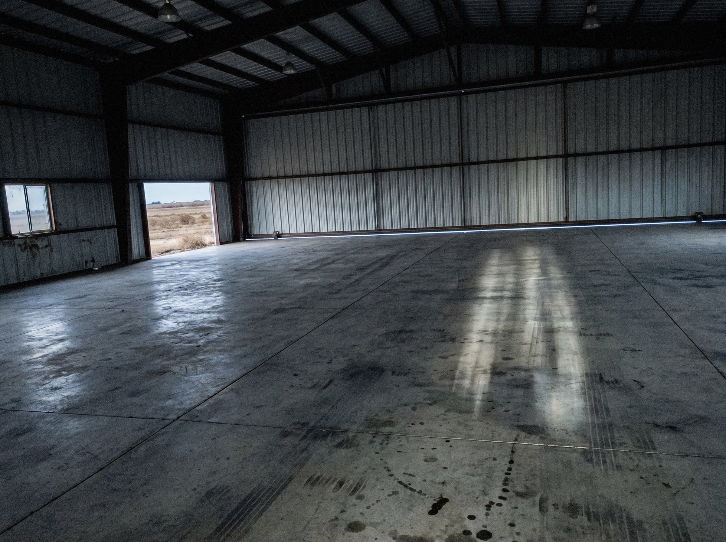 Empty hangar bay at first light, the door still closed, bare slab and no airplane