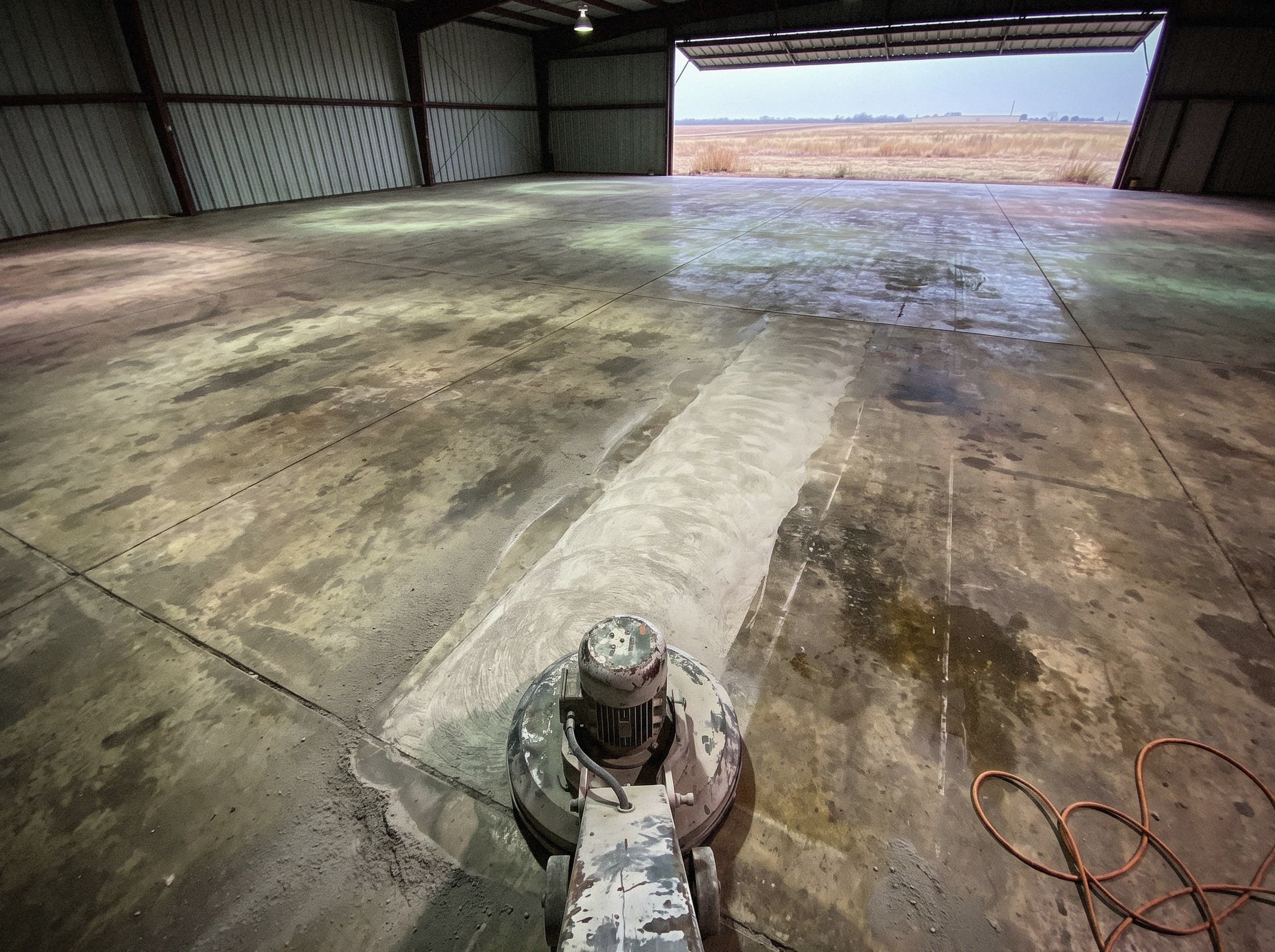 Grinding head on a hangar slab, a pale open strip of ground concrete beside the older darker floor