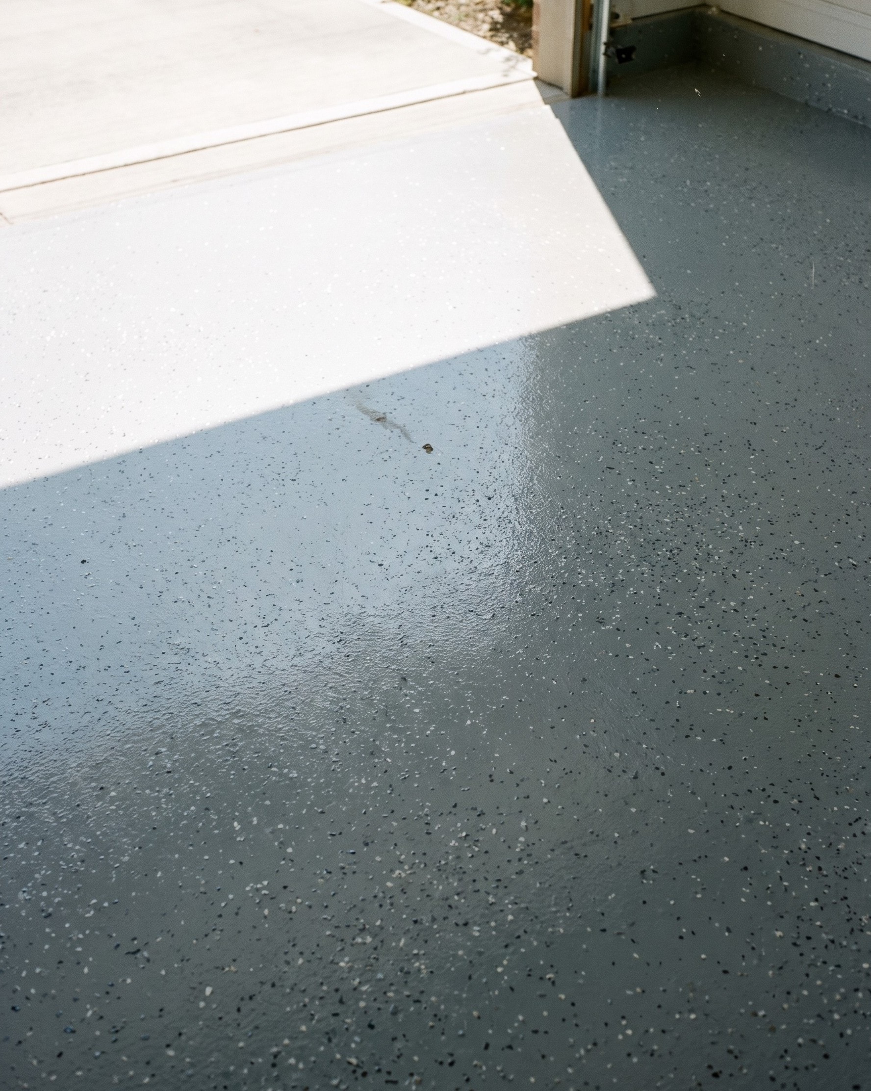 Afternoon sunlight falling through an open garage door across the first few feet of a gray flake floor, with a crisp shadow line where the sunlit strip ends