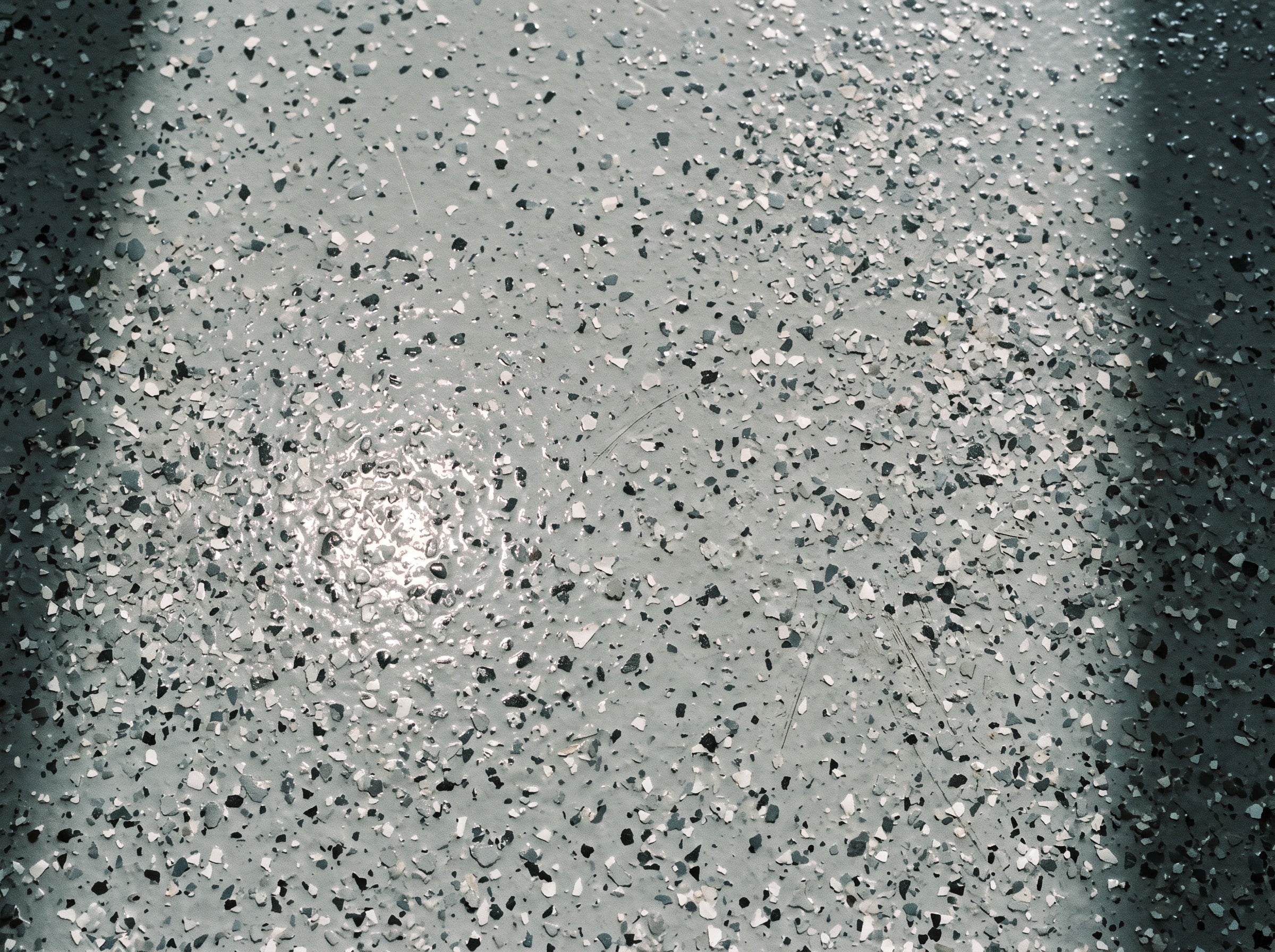 Top-down detail of a full-broadcast flake floor under a clear coat, about half a square meter, in daylight