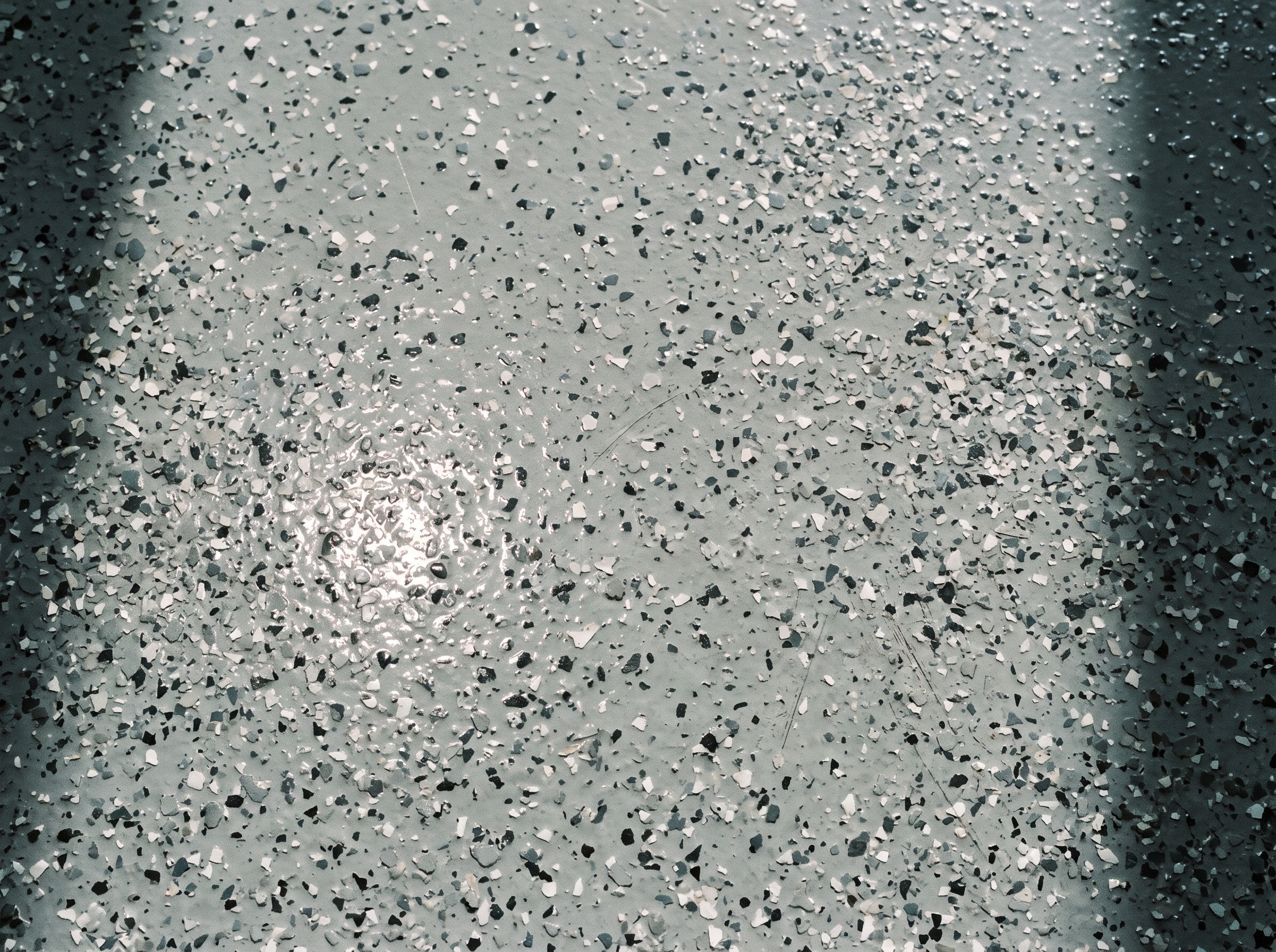 Top-down detail of a full-broadcast flake floor under a clear coat, about half a square meter, in daylight