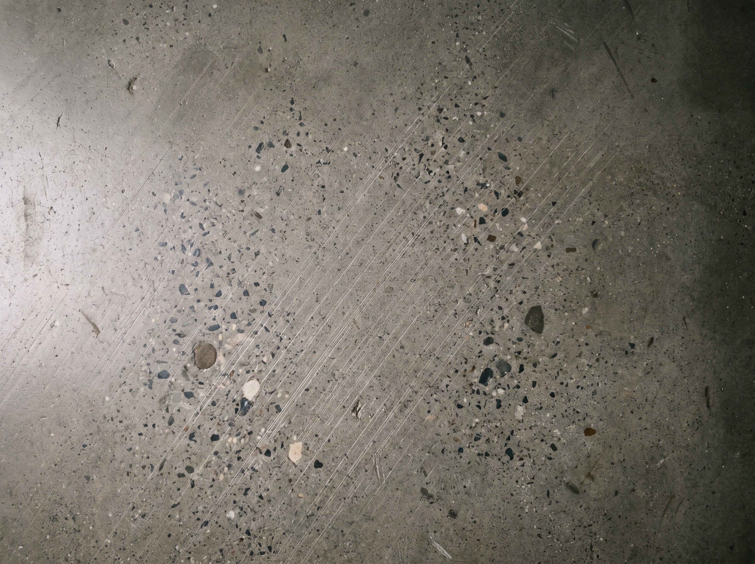 Top-down detail of a polished concrete floor with a soft sheen and light aggregate showing, about half a square meter, in daylight