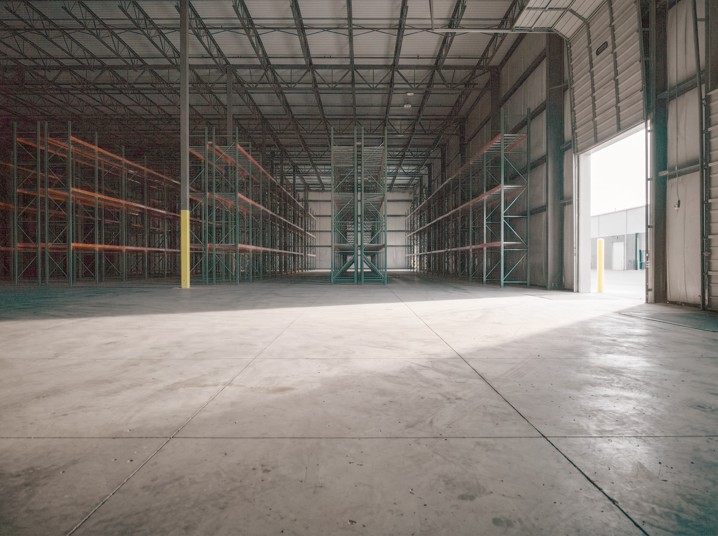 Empty distribution warehouse at first light, dock door rolled up, bare slab